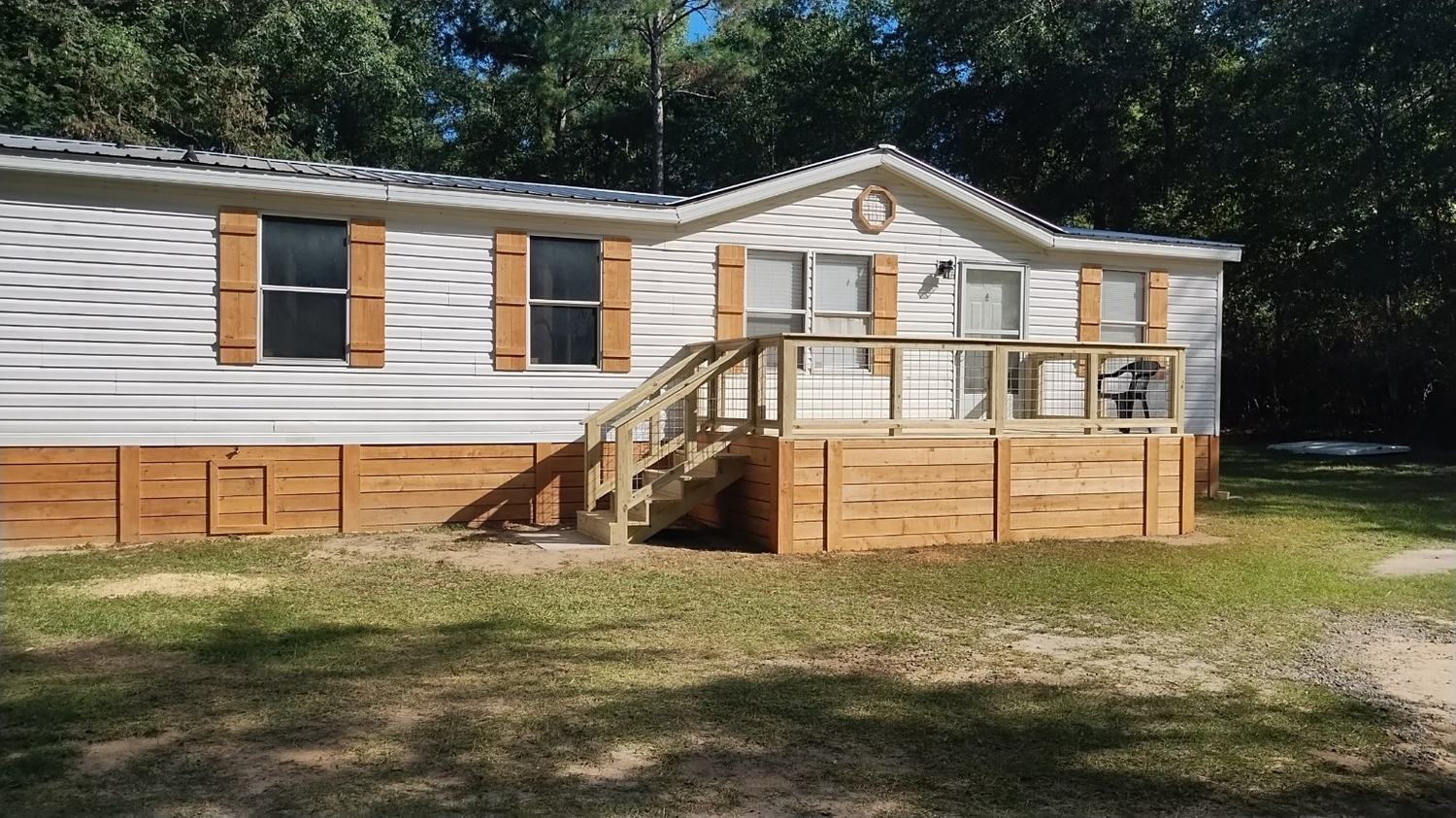Completed exterior carpentry with deck, railing, shutters, and skirting on a home.