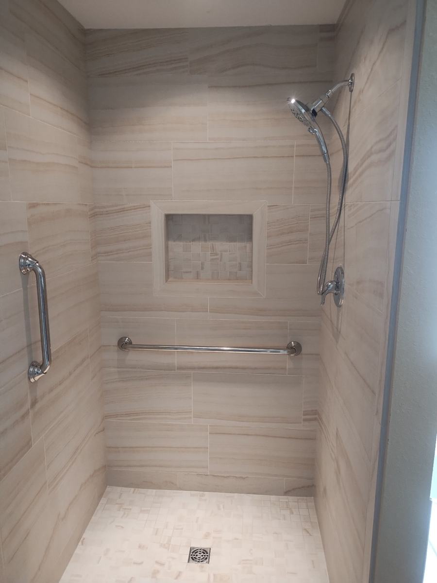 Completed tile shower with niche, shower head, grab bars, and tiled floor.
